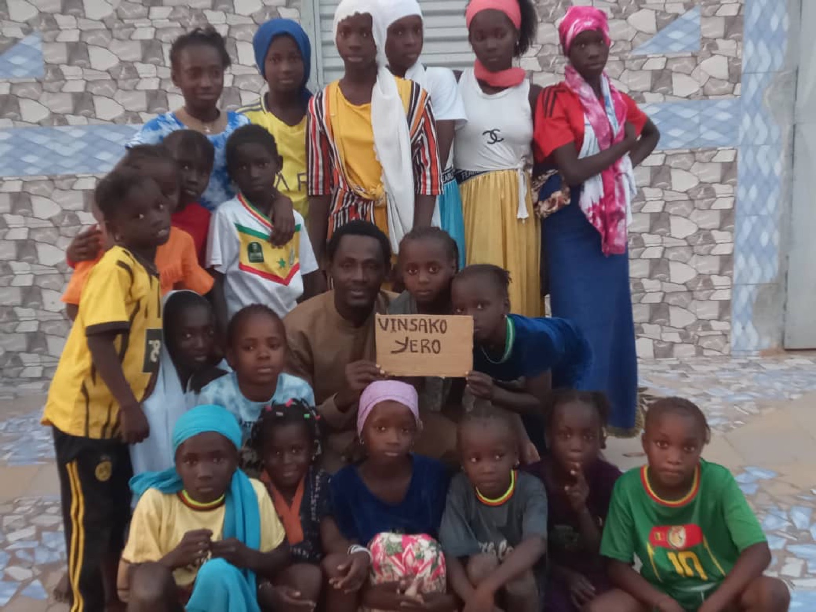 Arouna with the children of Vinsako Yero, holding a sign with the village name.